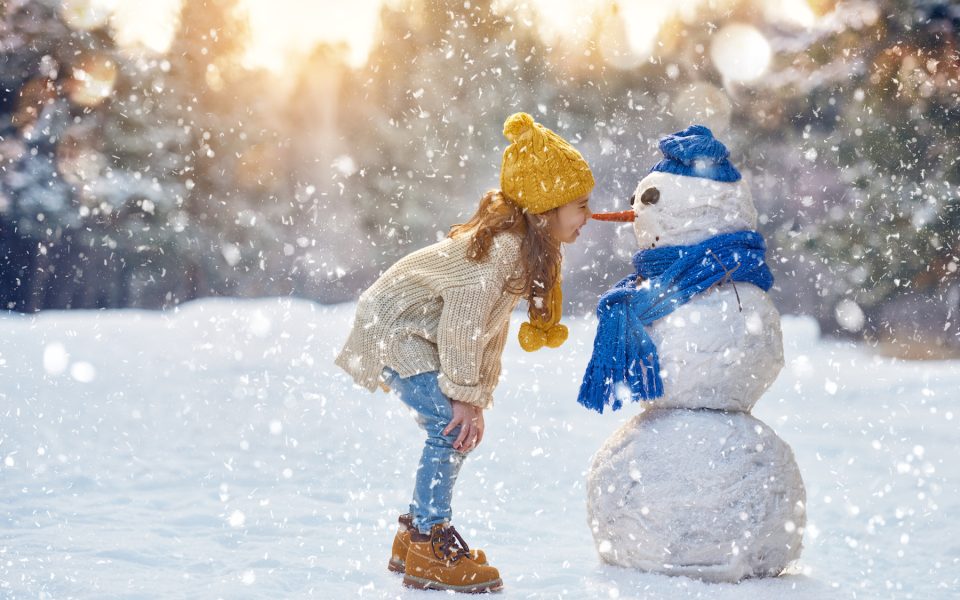 happy child girl plaing with a snowman on a snowy winter walk